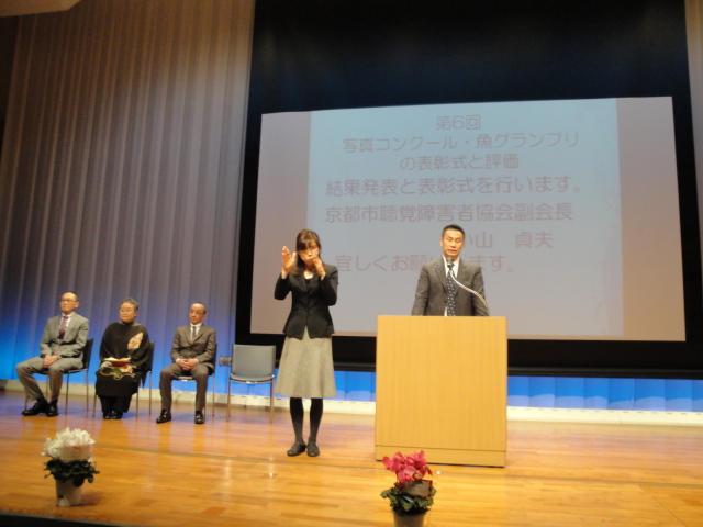 満席のホールでの表彰式で 後援団体の挨拶をする鎌谷会長